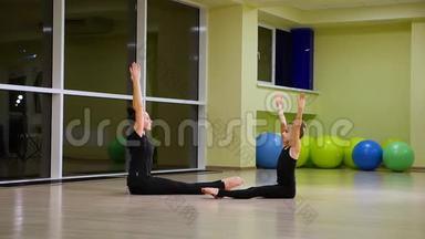 两个身材苗条、可爱的女孩姐妹，穿着黑色运动服的艺术体操运动员，在健身房做热身运动，做肌肉伸展运动